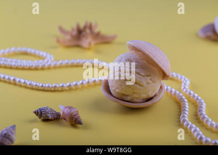 Con gelato alla vaniglia come pearl in conchiglia di mare su giallo Sfondo sabbia profondo mare perla collana spazio per il testo Foto Stock