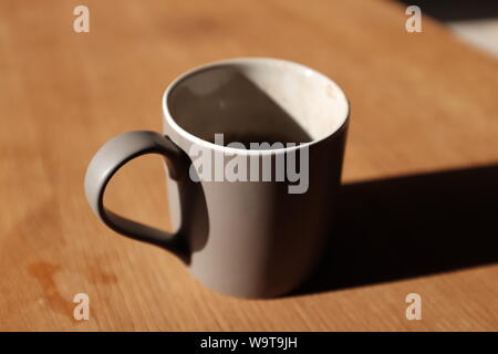 Una semi-finito di caffè in una tazza di colore grigio, colata di una lunga ombra su un tavolino una mattina d'estate. Foto Stock