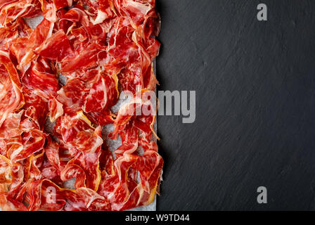 Stuzzicanti fette di prosciutto iberico in primo piano. Olio d'oliva. Sfondo nero. Spazio per inserire il tuo testo. Foto Stock