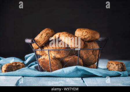 Panini di segale con i dadi in un cestello di ferro su un blu asciugamano da cucina e un tavolo di legno. Pronto a mangiare la prima colazione focacce di pane in un cestino. Foto Stock