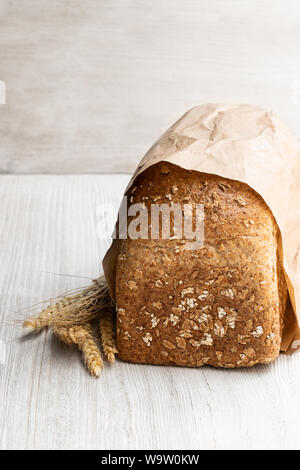 In casa pane integrale con fiocchi di avena in sacchetto di carta bianca sul tavolo di legno Foto Stock