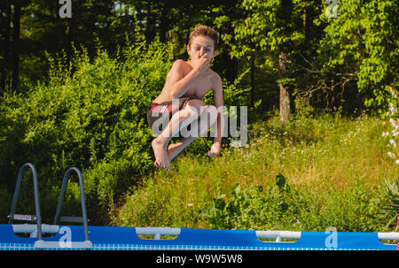 Un 12-anno vecchio ragazzo salti in una piscina mentre si collega il suo naso. Foto Stock