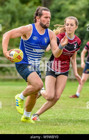 Giovane maschio (età 20-30) sprint in avanti con la palla in mano mentre il giovane giocatore femmina (età 14-20) tratti di toccare affrontare Foto Stock