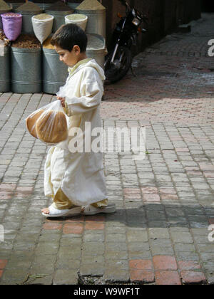 Marrakech Maroc Aprile 02,2010: giovane ragazzo marocchino in bianco abiti tradizionali e grandi scarpe è camminare nel souk e porta pane arabo Foto Stock