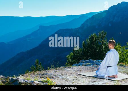 Karate master meditando sulla cima di una montagna di indossare il kimono mentre guardando giù al lago di montagna. Foto Stock