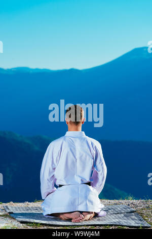 Karate master meditando sulla cima di una montagna di indossare il kimono mentre guardando giù al lago di montagna. Foto Stock