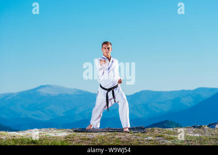 Bionda atleta di karate non kata sulla cima di una montagna mentre si esegue una linea di calci, pugni e blocchi sulla cima di una montagna in una giornata di sole. Foto Stock