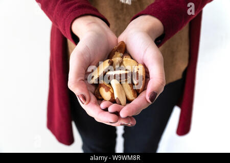 Stretta di mano ragazza con unghie verniciate azienda noci del Brasile (Bertholletia excelsa) su sfondo bianco. Le noci del Brasile sono molto nutriente e gustosa Foto Stock