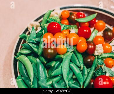 Colpo di closeup di un piatto riempito con broccoli, piselli verdi e pomodori ciliegini Foto Stock