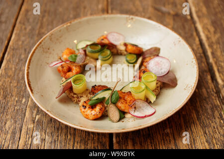 Antipasto con gamberetti, verdure e quinoa sul vecchio tavolo in legno, luce calda Foto Stock