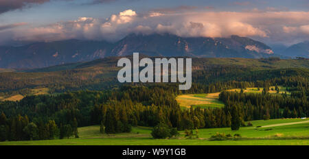 Panorama dei Monti Tatra. Picchi di montagna svettante su verdi colline erbose. Al di sopra dei picchi, bella nuvole temporalesche illuminato dall'impostazione s Foto Stock