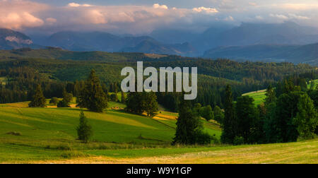 Panorama dei Monti Tatra. Picchi di montagna svettante su verdi colline erbose. Al di sopra dei picchi, bella nuvole temporalesche illuminato dall'impostazione s Foto Stock
