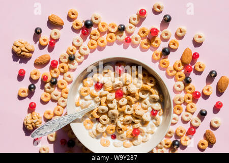 Fiocchi di cereali integrali con i frutti di bosco e latte sul rosa. Una sana colazione gustosa cornflakes con mirtilli, lamponi e ribes rosso.Multigrain Foto Stock