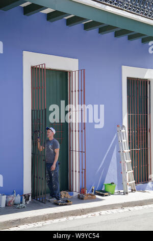 Un imbianchino funziona sulla porta di ferro di ante con tutti i suoi strumenti previsti dalla parete dipinta nel pomeriggio soleggiato, San Juan Vecchia San Juan, Puerto Rico. Foto Stock