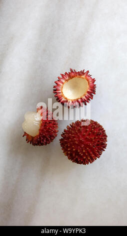 Frutti Pulasan - uno intero e un altro pelato. Nome scientifico Nephelium ramboutan-akea, pulasan è un rosso di frutta tropicale strettamente alleati di rambutan. Foto Stock