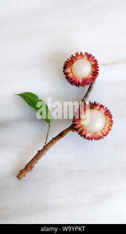 Piatto di laici pulasan frutta, foglie e rami disposti in un disegno floreale. Pulasan è un rosso di frutta tropicale dal sud-est asiatico. Foto Stock