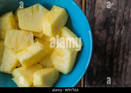 Primo piano di pezzi di ananas tagliati in una ciotola blu su sfondo di legno Foto Stock