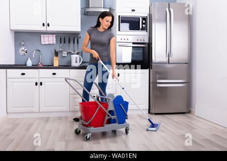 Felice bidello femmina piano di pulizia con Mop in cucina Foto Stock