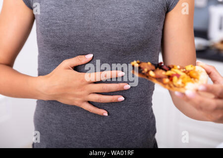 Close-up di una donna che tiene un trancio di pizza e sfrega il suo ventre Foto Stock