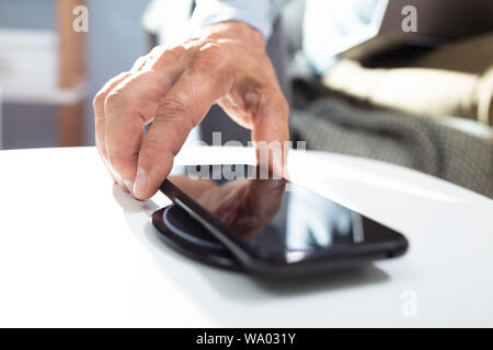 Uomo in carica lo smartphone utilizzando Wireless Pad di ricarica a casa Foto Stock