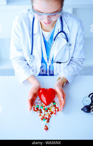 Pillole colorate su un tavolo a forma di cuore su uno sfondo bianco e il tonometro. Cuore rosso . Dottore le mani sul tavolo vicino al cuore e pillola Foto Stock