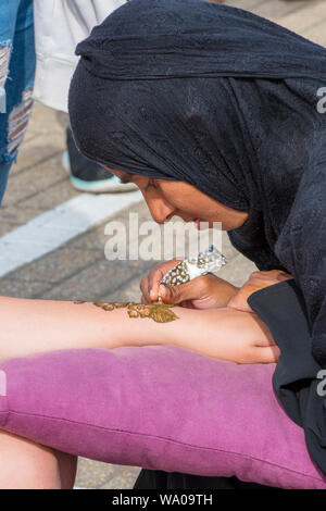 Un indiano di religione musulmana o tattooist asiatici creando un henna tattoo sul braccio e indossa una cappa. Foto Stock