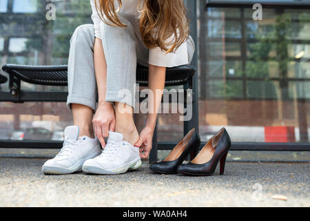 Close-up di imprenditrice è seduta sul banco di indossare scarpe comode Foto Stock