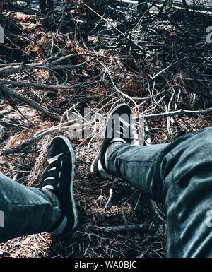 I piedi della persona in jeans e sneakers neri sui ramoscelli dentro una foresta Foto Stock