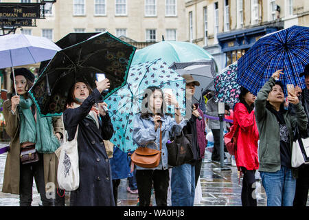 Bagno, Somerset, Regno Unito. Il 16 agosto, 2019. I turisti il ricovero sotto gli ombrelli da pioggia heay sono illustrati come loro di scattare fotografie di Abbazia di Bath come heavy rain docce fanno la loro strada attraverso il Regno Unito. Credito: Lynchpics/Alamy Live News Foto Stock