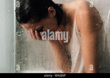 Lonely premuto donna che piange nella doccia attraverso il vetro con gocce d'acqua Foto Stock