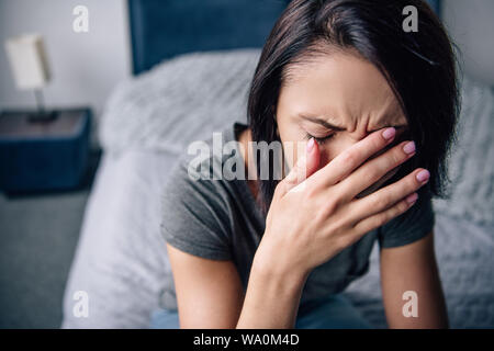 Premuto donna seduta sul letto di casa piangendo e che copre il viso con le mani Foto Stock