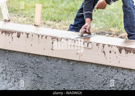 Lavoratore edile con frattazzo su cemento umida di coping di formazione intorno alla nuova piscina. Foto Stock