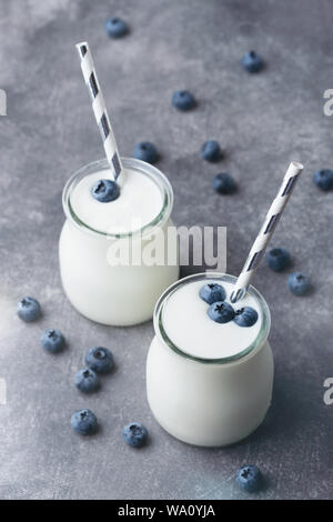 Lo yogurt greco con mirtilli in un vaso di vetro con carta paglia su sfondo grigio. Una sana alimentazione e dieta concetto. Primo piano. Foto Stock