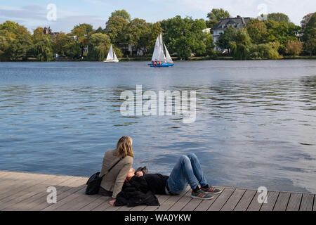Coppia giovane seduto sul molo guardando la gara di barche a vela sul lago Alster,Amburgo, Germania Foto Stock