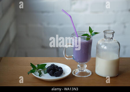 Close up frullato di blackberry in un bicchiere di vetro e una bottiglia di latte e un piattino con frutti di bosco freschi e un rametto di menta, il fuoco selettivo Foto Stock