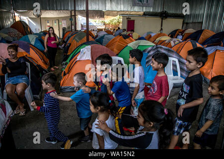 12 agosto 2019, Messico, Tijuana: i bambini migranti in coda fino al 'Juventud 2000' ostello per lezioni con i giovani dal 'Angeles de la frontera " gruppo. Le visite di gruppo tre ostelli migranti in Messico città di confine di Tijuana con un bus di scuola. Là il gruppo lavora ogni settimana con circa 150 i bambini migranti. "Qualsiasi hanno difficoltà di lettura e di scrittura,' afferma il project leader Andrea Rincon, che attribuisce queste difficoltà per la mancanza di pratica. Gruppo messicano ha contattato l'organizzazione del progetto Schoolbox ed ora i piani per implementare la sua esperienza con i bambini migranti in Grecia Foto Stock