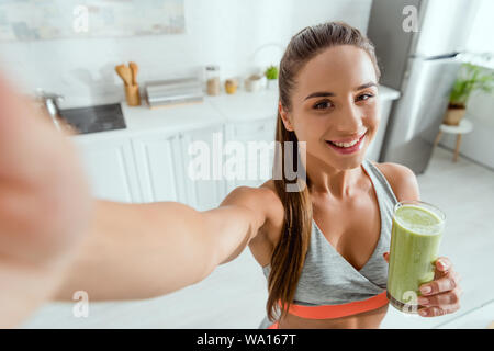 Messa a fuoco selettiva di felice ragazza con frullato di verde e guardando la fotocamera Foto Stock