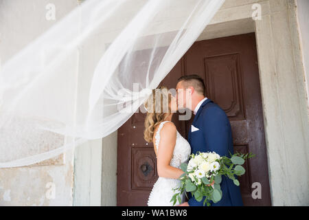 Il bacio. Sposa e lo sposo baci teneramente nell'ombra di un velo di volo. Artistico in bianco e nero foto di matrimonio. Foto Stock