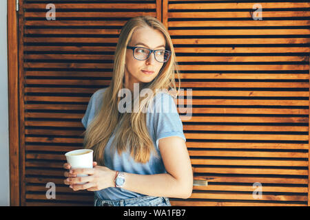 Biondo con gli occhiali con un bicchiere di carta di caffè all'interno Foto Stock