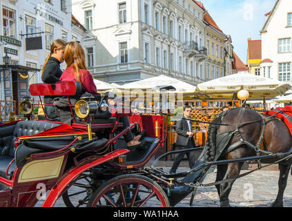Due giovani donne estone di guidare un turista carro trainato da cavalli parlare tra di loro nella piazza del Municipio di Tallinn medievale, Estonia Foto Stock