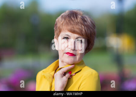 Bella donna anziana in abiti di colore giallo in un parco della città. Foto Stock