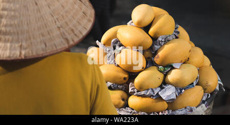 La città di Ho Chi Minh, Vietnam - Gennaio 9, 2019: un venditore ambulante in un cappello conico vende mango al mercato. Foto Stock