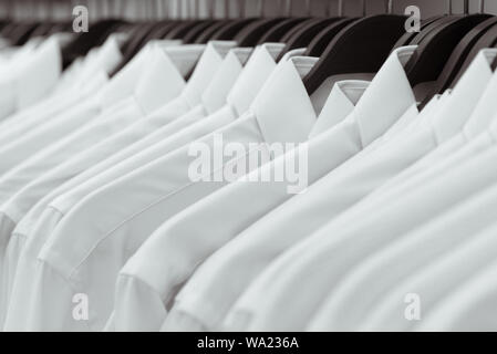 Fila di camicie bianche appendere su appendiabiti nero su un rack in un negozio. Un close-up. Foto Stock