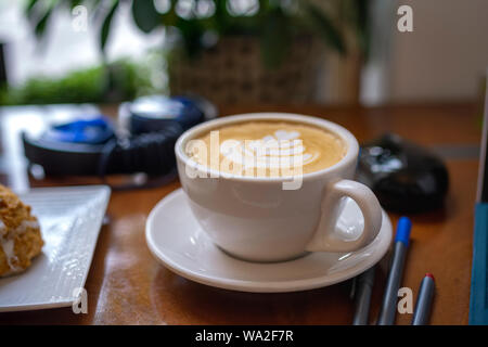 Studiare con un delizioso cappuccino circondato da materiali di studio e di elettronica. Foto Stock