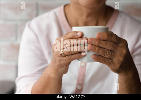 Vecchia donna detiene una tazza di caffè caldo bere a casa Foto Stock