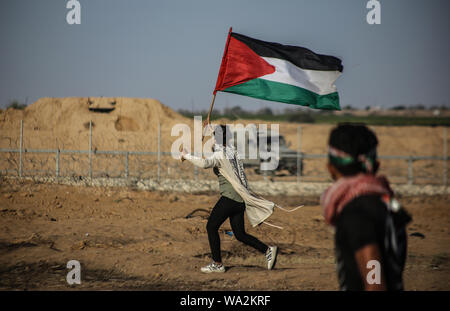 Un manifestante palestinese sventola la bandiera palestinese durante gli scontri tra dimostranti palestinesi e israeliane attraverso la recinzione tra Gaza e Israele vicino a Khan Younis nel sud della striscia di Gaza pur dimostrando impegnativo il sollevamento dell'assedio imposto sulla cittadinanza per anni. Foto Stock