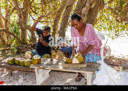 Lifou, Nuova Caledonia - 9 Gennaio 2014: Donna e figlio la preparazione di noci di cocco per la vendita. Nave da crociera il turista a godere di bere succo di cocco. Foto Stock