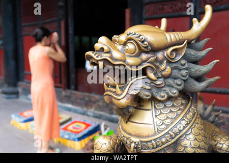 La testa di un Leone d'oro statua al monastero di Wenshu e sfocata donna cinese pregando di unire le vostre mani in background in Chengdu Sichuan in Cina Foto Stock