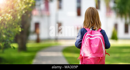 Ragazza con zaino infront di un edificio scolastico Foto Stock