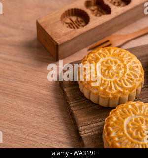 Una forma rotonda sfornato fresco torta della luna - pasticceria Cinese per moonckae Mid-Autumn Festival di luna su sfondo di legno e serve il vassoio, close up, spazio di copia Foto Stock